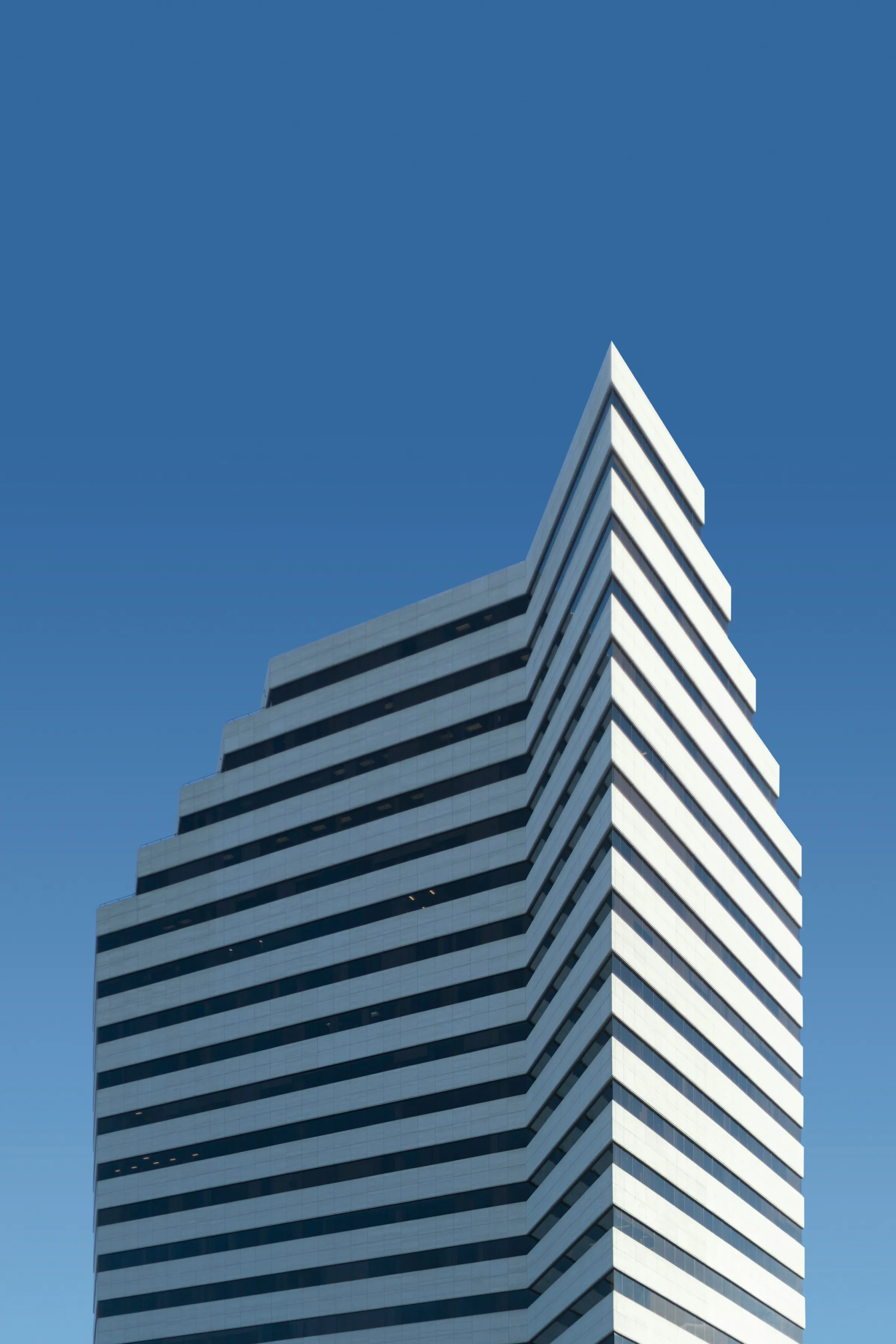 A stepped white skyscraper with a sharp angular crown against a deep blue sky.