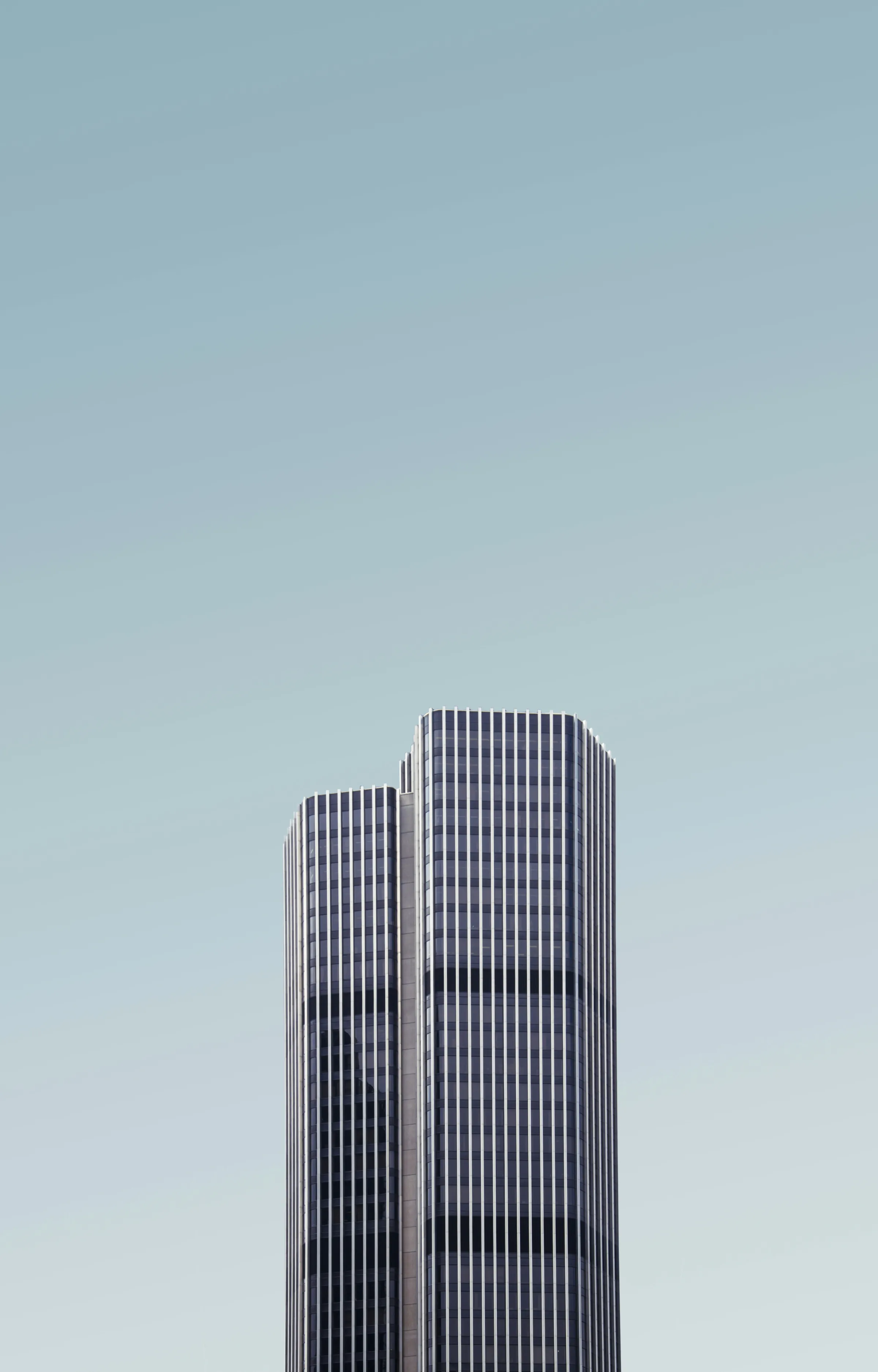 A twin-tower skyscraper with vertical window fins against a pale grey-blue sky.