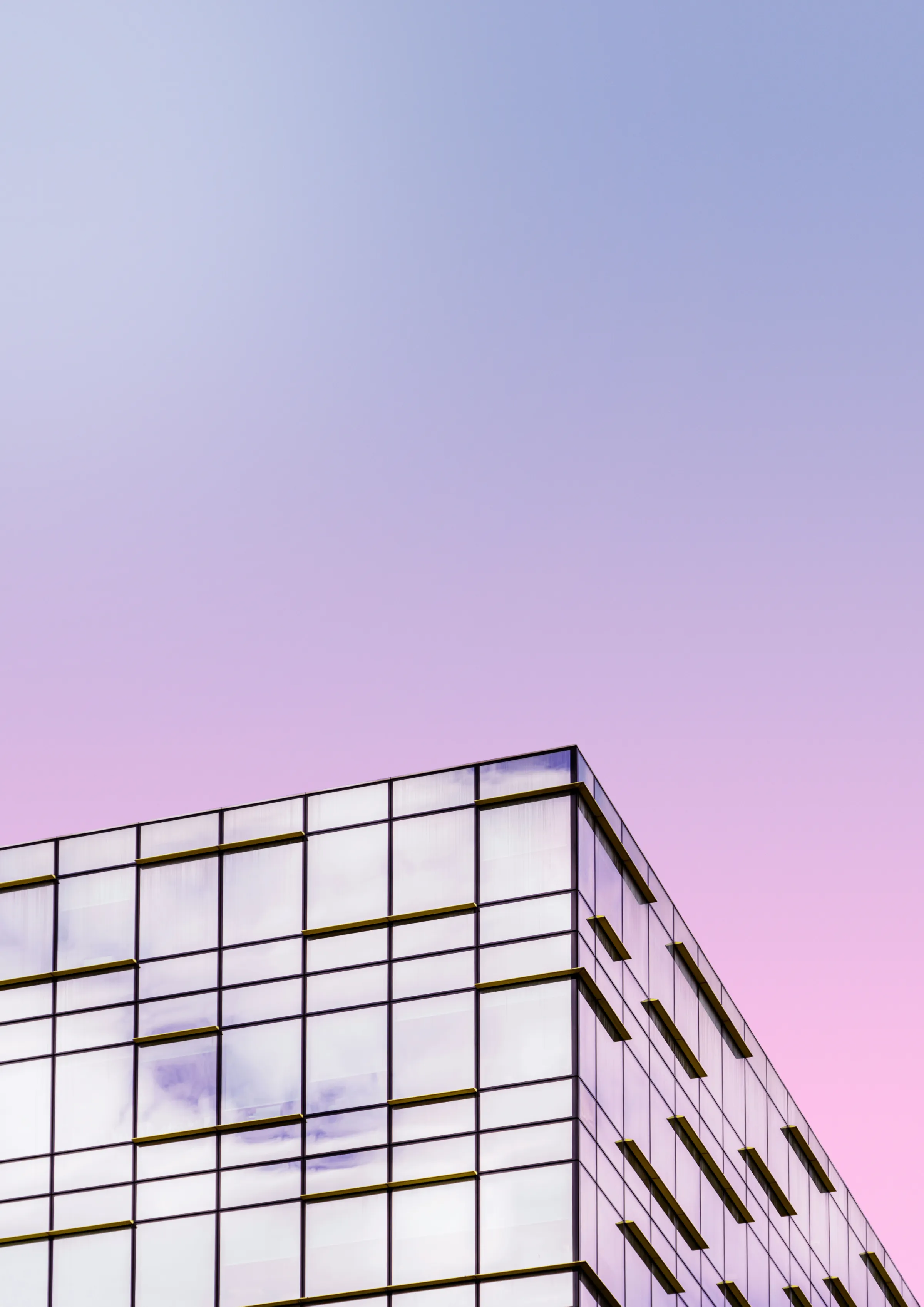 The corner of a gridded glass office building against a pastel pink-and-lilac sunset sky.