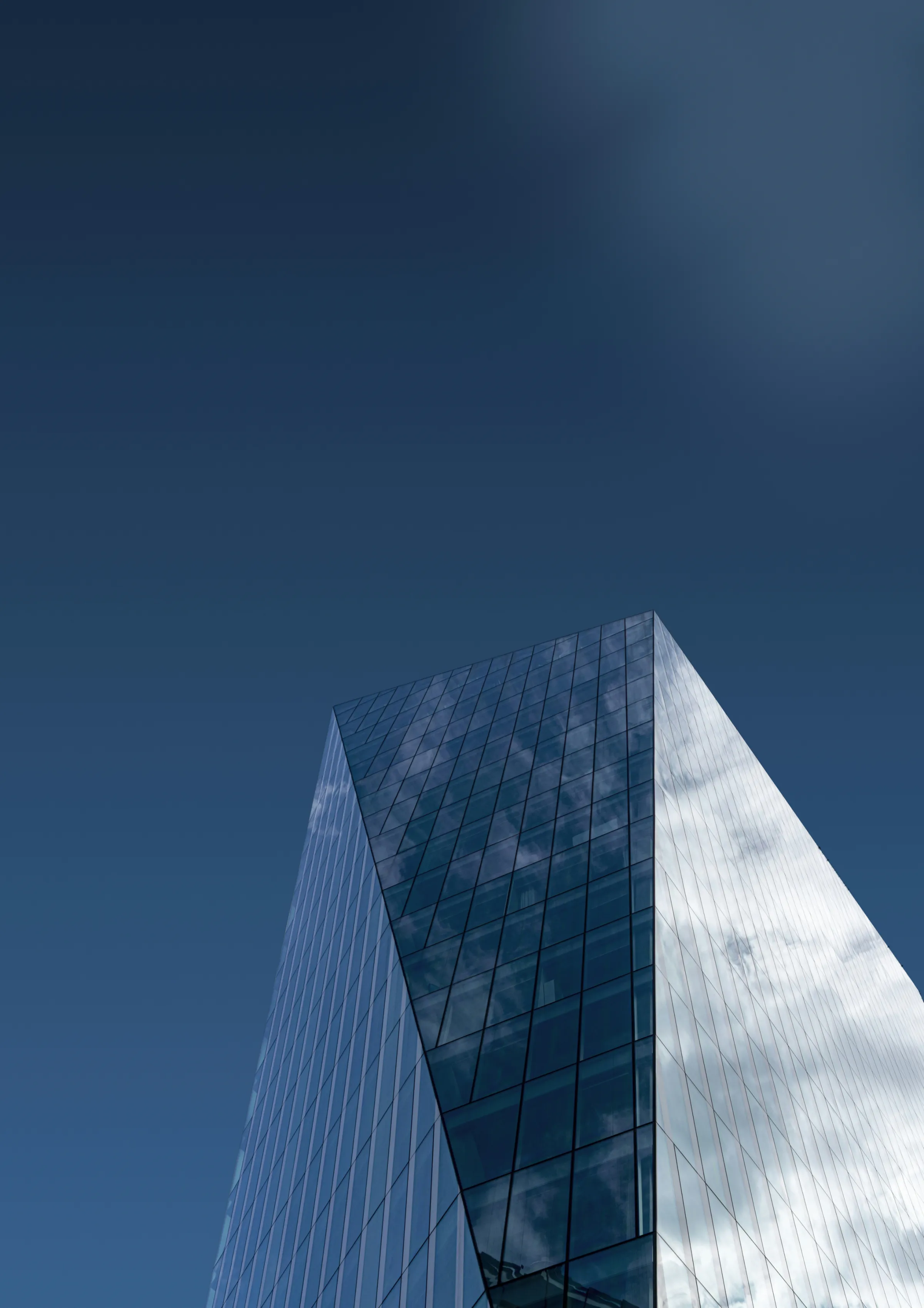 A dark blue glass skyscraper corner reflecting clouds against a deep navy sky.