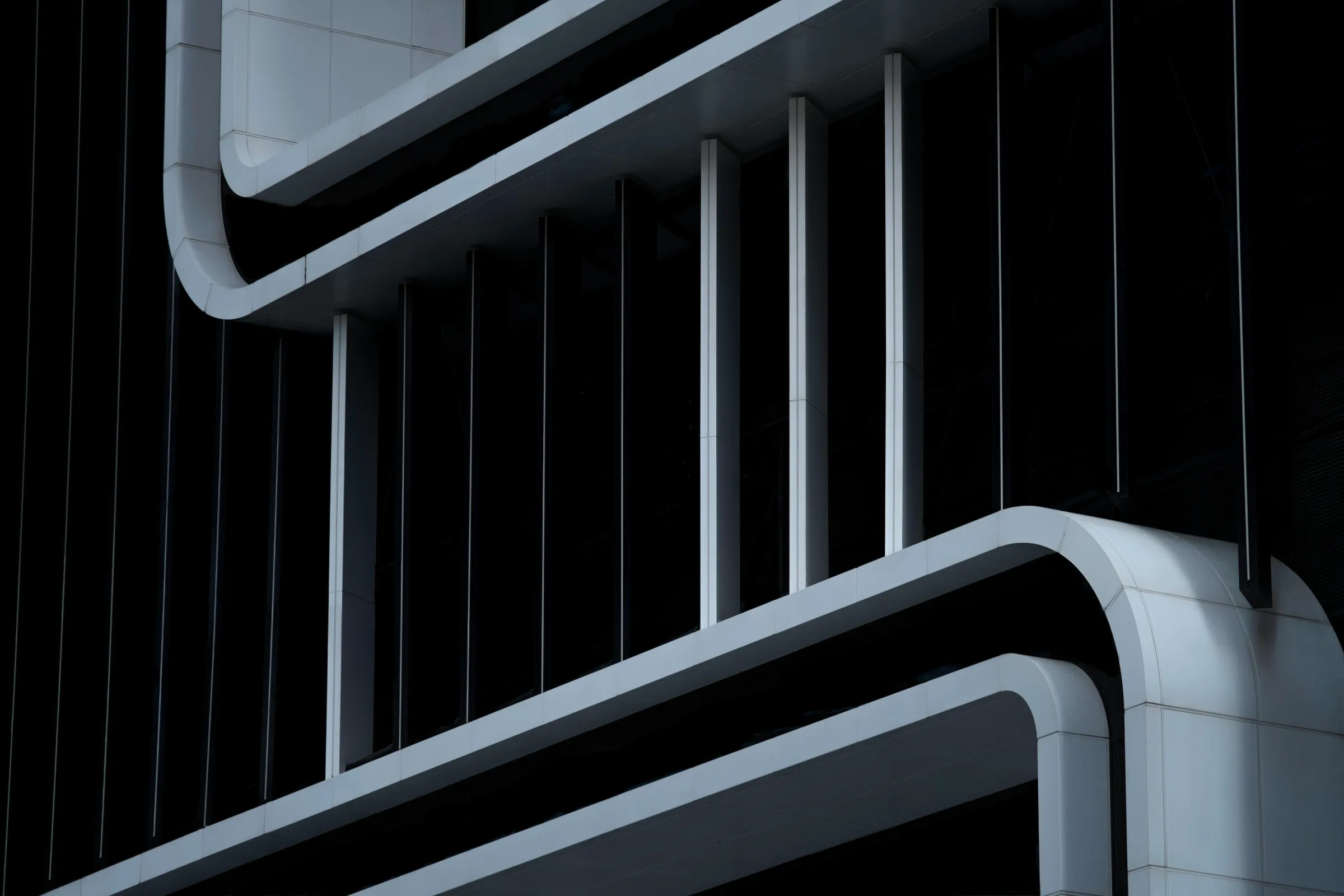 Abstract close-up of a white curved architectural facade with vertical fins against deep black shadow.