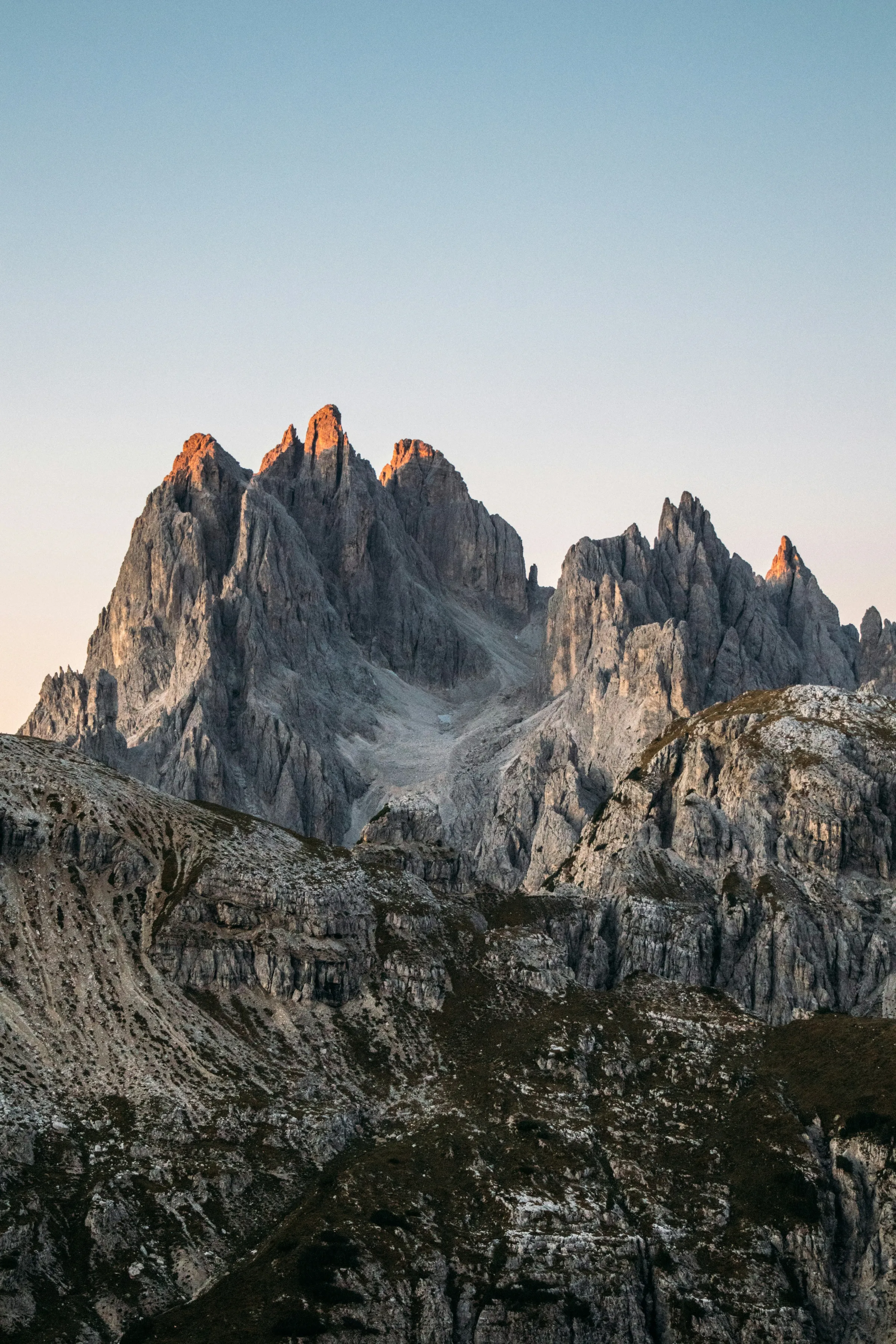 Jagged grey Dolomite mountain peaks catching orange sunrise light against a pale blue sky.