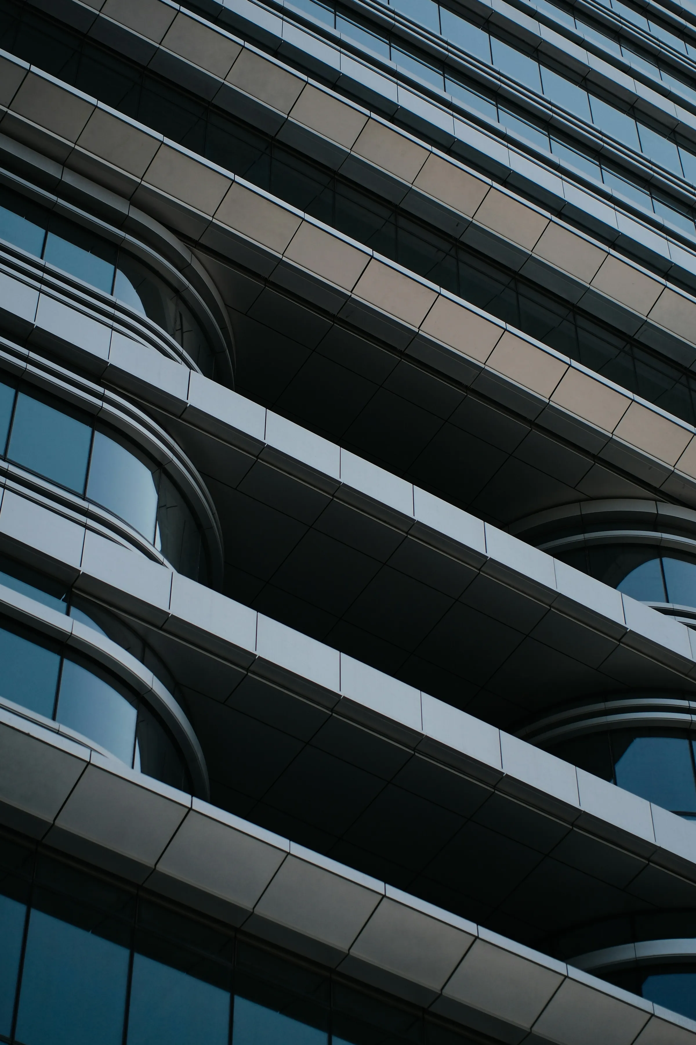 Close abstract view of a modern skyscraper facade with horizontal balcony bands and curved glass balconies in blue-grey tones.