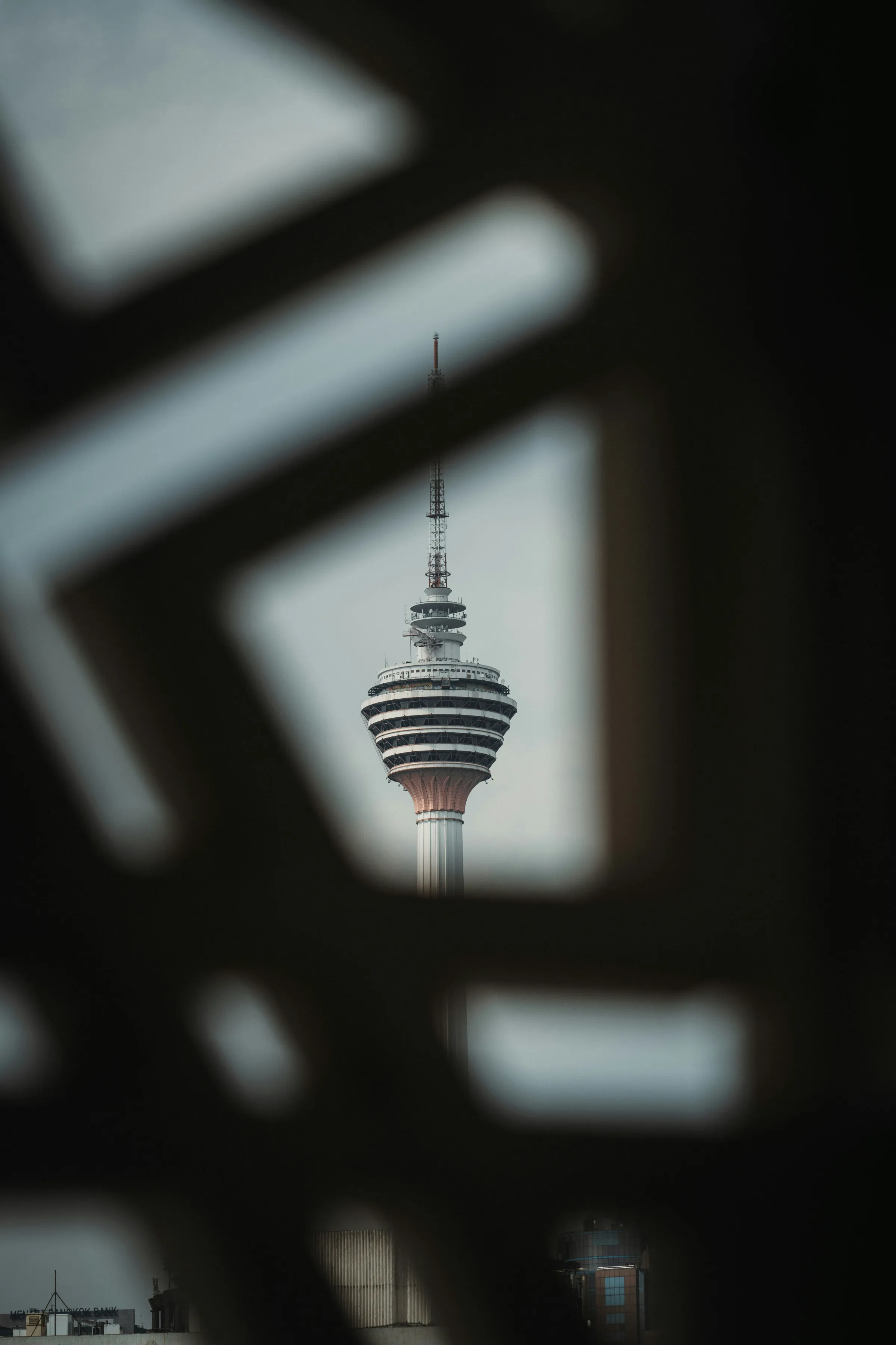 The Kuala Lumpur Tower framed through the diamond gaps of a dark out-of-focus decorative screen.