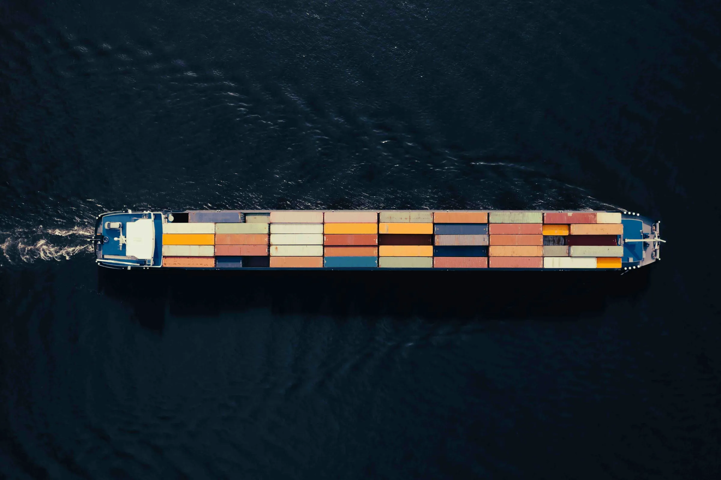 Aerial top-down view of a container ship carrying colourful stacked containers on dark navy water.